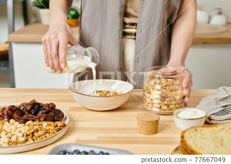 A woman pouring milk into bowl with corn flakes A woman pouring milk into bowl with corn flakes 77667049