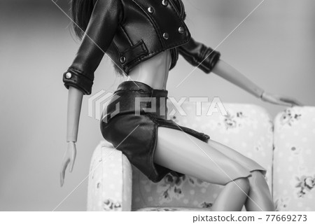 Closeup of brunette mannequin doll wearing leather skirt and leather jacket sitting on sofa in outdoor 77669273