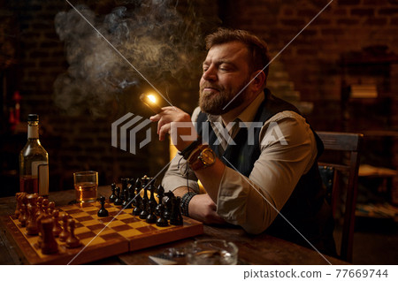 Man smokes a cigar, smoker leisures at chessboard Man smokes a cigar, smoker leisures at chessboard 77669744