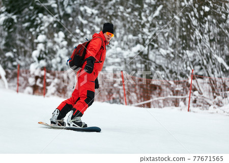 Male snowboarder in a red suit rides on the snowy hill with snowboard, Skiing and snowboarding concept Male snowboarder in a red suit rides on the snowy hill with snowboard, Skiing and snowboarding concept 77671565