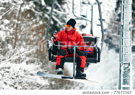 Skier sitting at ski lift talking on the phone in high mountains during sunny day. Winter sport and recreation, leisure outdoor activities. Skier sitting at ski lift talking on the phone in high mountains during sunny day. Winter sport and recreation, leisure outdoor activities. 77671567