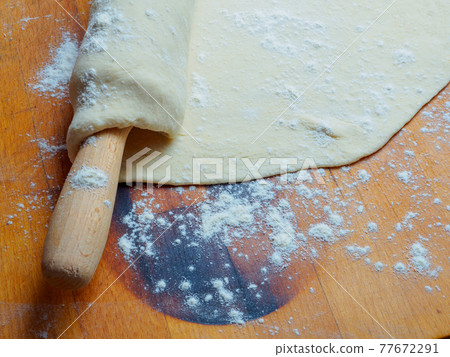 Pizza dough base wrapped on a rolling pin on a wooden table sprinkled with flour 77672291