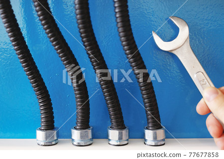These are power cables in corrugated insulation and a rock electrician with a wrench close up against a blue wall These are power cables in corrugated insulation and a rock electrician with a wrench close up against a blue wall 77677858