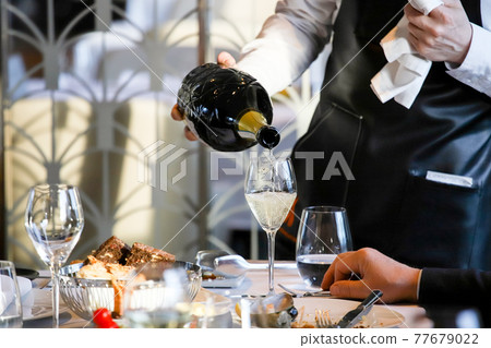 The waiter pours white wine into a glass. Banquet, cutlery, table setting. 77679022