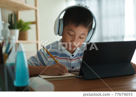 Asian boy learning online via internet with a tutor on a tablet digital with headphone Asian boy learning online via internet with a tutor on a tablet digital with headphone 77679055