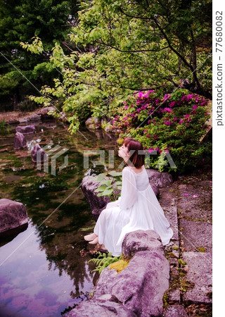 一個穿著白裙的女人站在公園裡” 77680082