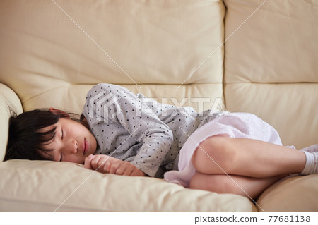 An elementary school girl taking a nap on the sofa in the living room 77681138