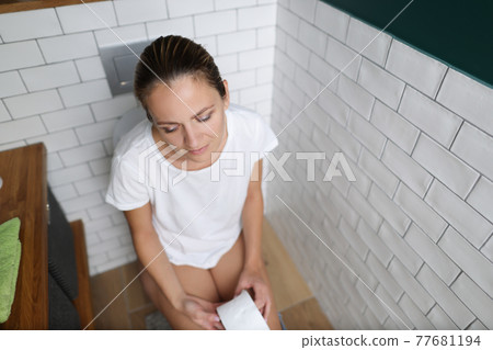 Young woman is sitting on toilet with her eyes closed Young woman is sitting on toilet with her eyes closed 77681194