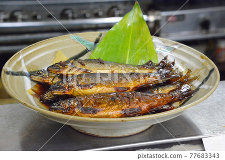At the sushi restaurant counter, a whole sweetfish boiled in sweetfish served on a large plate. 77683343
