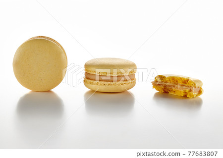 Two whole and one bitten macarons on white surface Two whole and one bitten macarons on white surface 77683807