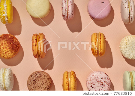 Top view of macarons symmetrically arranged with one missing in center on pink background 77683810