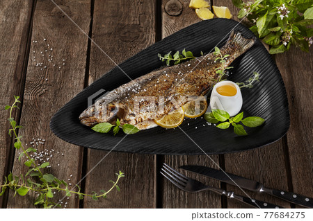 Grilled rainbow trout with lemon and herbs on wooden table Grilled rainbow trout with lemon and herbs on wooden table 77684275