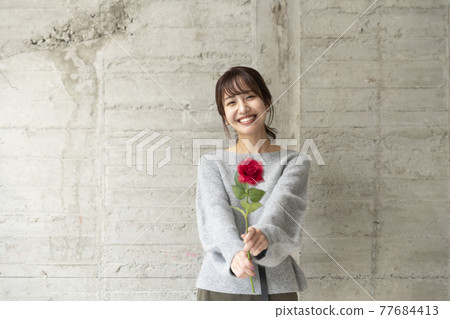 一個年輕女子在混凝土牆前拿著一朵玫瑰 77684413