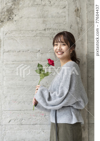 一個年輕女子在混凝土牆前拿著一朵玫瑰 77684437