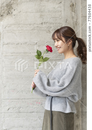 一個年輕女子在混凝土牆前拿著一朵玫瑰 77684438