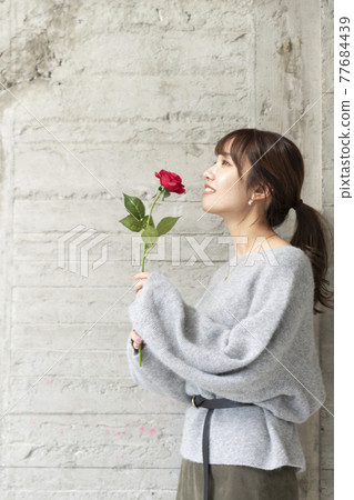 一個年輕女子在混凝土牆前拿著一朵玫瑰 77684439