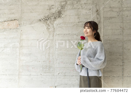 A young woman holding a rose in front of a concrete wall A young woman holding a rose in front of a concrete wall 77684472