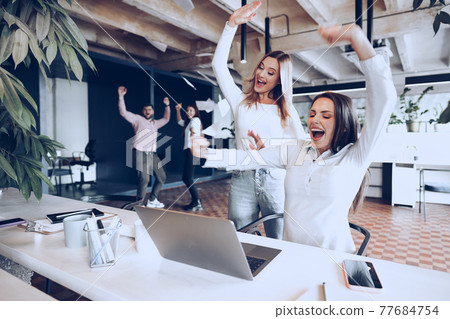 Two young happy businesswomen celebrating project success in office Two young happy businesswomen celebrating project success in office 77684754