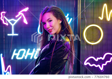 Portrait of a young attractive female standing near neon lamps at night Portrait of a young attractive female standing near neon lamps at night 77684760
