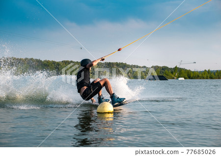 Wakeboarder making grab of board maneuvering between buoys 77685026