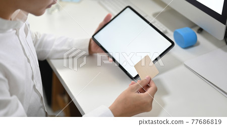 A young smart man is shopping online with a computer tablet at the white working desk. 77686819