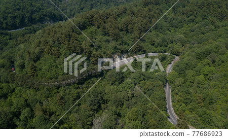 Aerial view from above of curve road with a car on the mountain with green forest in Russia 77686923