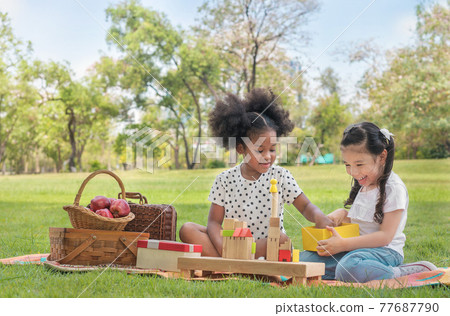 Happy cheerful ethnic girls play wooden block puzzle together at outdoors park , Relationship little kids, Diverse ethnic concept. 77687790