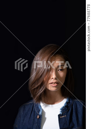 Face up of a young woman wearing a denim jacket on a white T-shirt on a black background 77688778