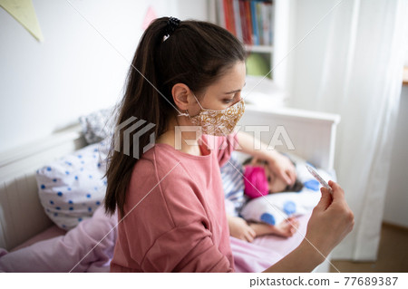 Mother looking after sick small daughter in bed at home, coronavirus concept. 77689387