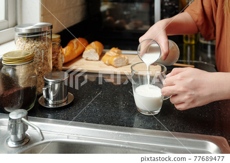 Woman pouring milk in glass 77689477