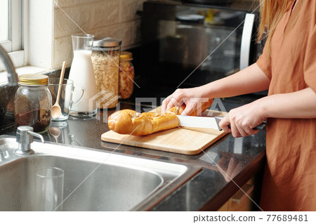 Housewife cutting baguette 77689481