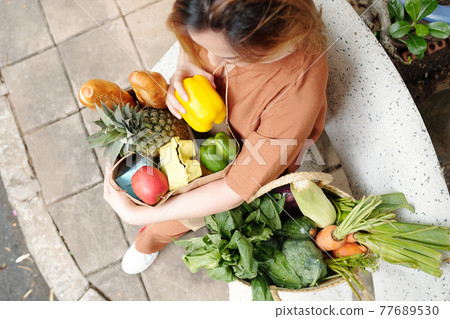 Woman sitting on bench with grocery bags 77689530