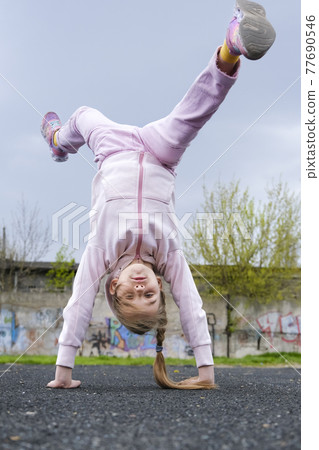 Teenage girl doing a handstand on the background of the stadium. The child girl goes in for sports and gymnastics Teenage girl doing a handstand on the background of the stadium. The child girl goes in for sports and gymnastics 77690546