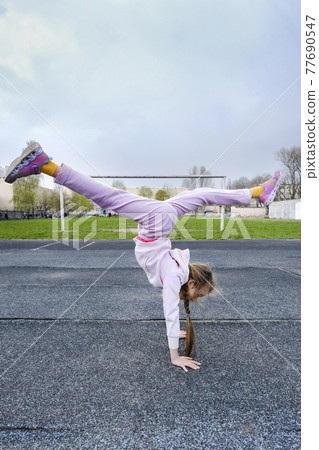 Teenage girl doing a handstand on the background of the stadium. The child girl goes in for sports and gymnastics Teenage girl doing a handstand on the background of the stadium. The child girl goes in for sports and gymnastics 77690547