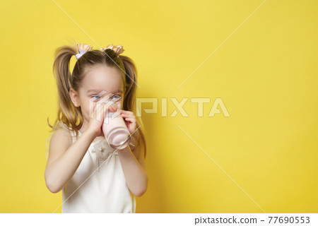 Little girl drinks yogurt from a glass isolated on yellow backdround. Healthy eating concept. Banner with copy space Little girl drinks yogurt from a glass isolated on yellow backdround. Healthy eating concept. Banner with copy space 77690553