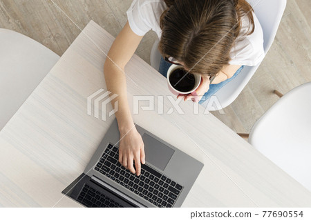 Top view on young Woman working on the laptop in modern place. Home office concept. Girl, laptop, table with coffee cup in modern coworking. Top view on young Woman working on the laptop in modern place. Home office concept. Girl, laptop, table with coffee cup in modern coworking. 77690554