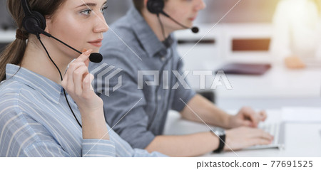 Call center. Group of casual dressed operators at work. Brunette business woman in headset at customer service office 77691525