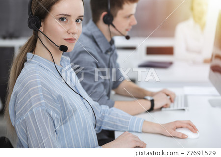 Call center. Group of casual dressed operators at work. Brunette business woman in headset at customer service office Call center. Group of casual dressed operators at work. Brunette business woman in headset at customer service office 77691529