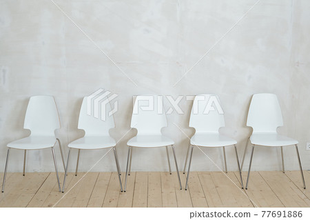 Row of white chairs near wall 77691886