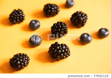Blackberries and blueberries on a yellow background Blackberries and blueberries on a yellow background 77692129