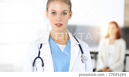 Woman - doctor is using clipboard for filling up medication history record form in sunny clinic at the background of patient Woman - doctor is using clipboard for filling up medication history record form in sunny clinic at the background of patient 77693264