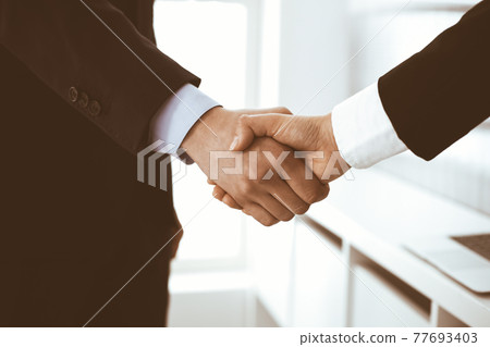 Businessman and woman shaking hands in office. Concept of handshake as success symbol in business 77693403