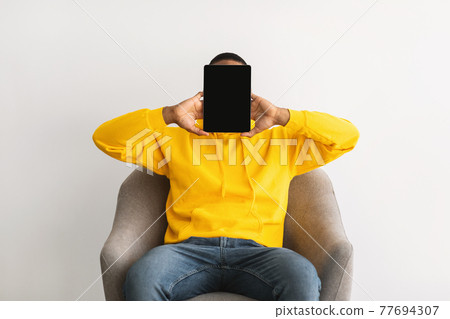 Black Man Holding Tablet Blank Screen Covering Face, Gray Background Black Man Holding Tablet Blank Screen Covering Face, Gray Background 77694307