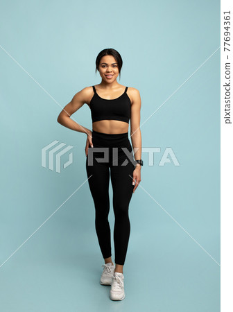 Happy fitness black model in sportswear standing isolated on blue background, studio shot. Happy fitness black model in sportswear standing isolated on blue background, studio shot. 77694361