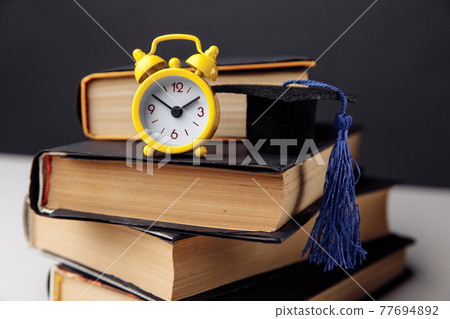 Yellow alarm clock, mini graduation cap and books on table. Education concept Yellow alarm clock, mini graduation cap and books on table. Education concept 77694892