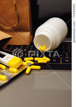 Bags with pills and drugs on a laptop keyboard. Buying medicines online theme. Vertical image 77695081