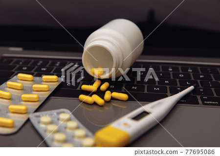 Health and medicine theme. Pills, thermometer and container on the keyboard laptop Health and medicine theme. Pills, thermometer and container on the keyboard laptop 77695086
