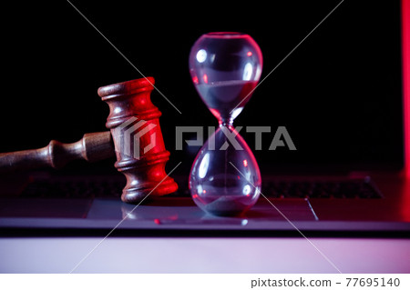 Judge's gavel, scales of justice and hourglass on laptop close-up. Online auction concept 77695140