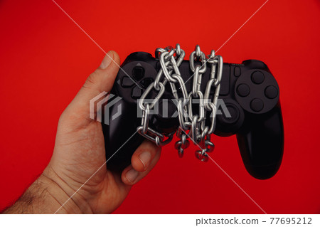 Young man holds a game controller is tied by chain isolated on red background 77695212
