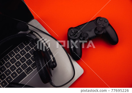 Laptop with headphones, gamepad on red background. Gaming and cybersport concept Laptop with headphones, gamepad on red background. Gaming and cybersport concept 77695226